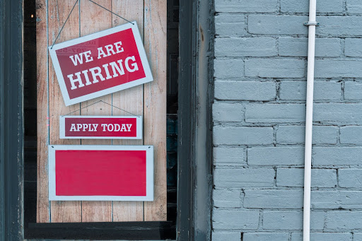 Red coloured ‘we are hiring’ signs posted on a window.