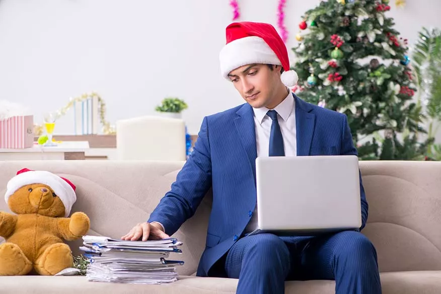 business man with santa hat working on his laptop with a stack of papers